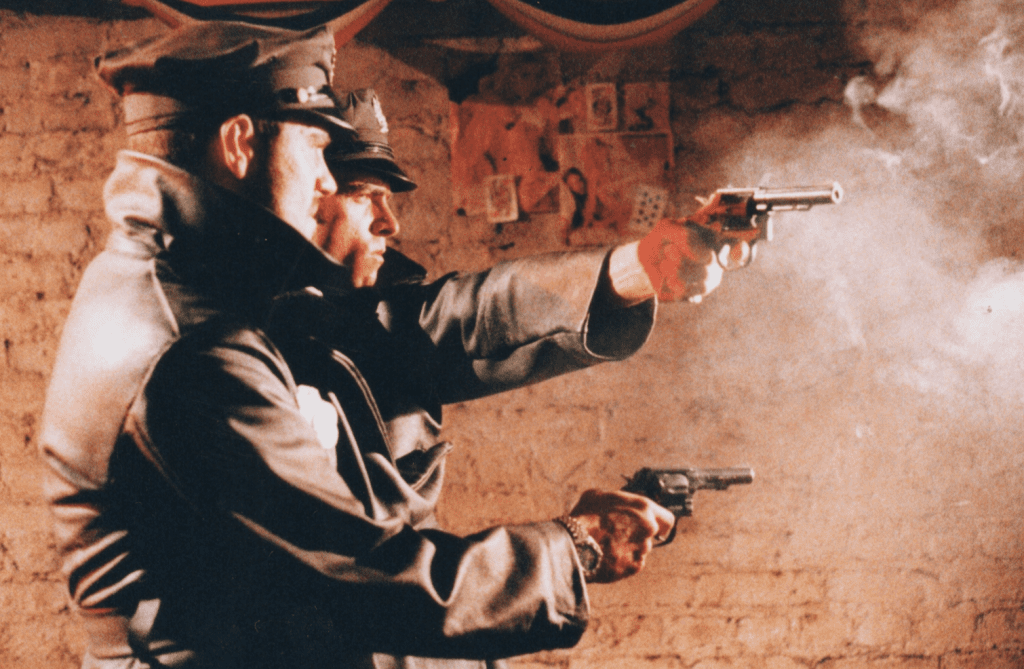 A Siamese Policeman with two guns being fired at the same time in a back street