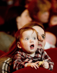 An amazed looking baby at a cinema screen